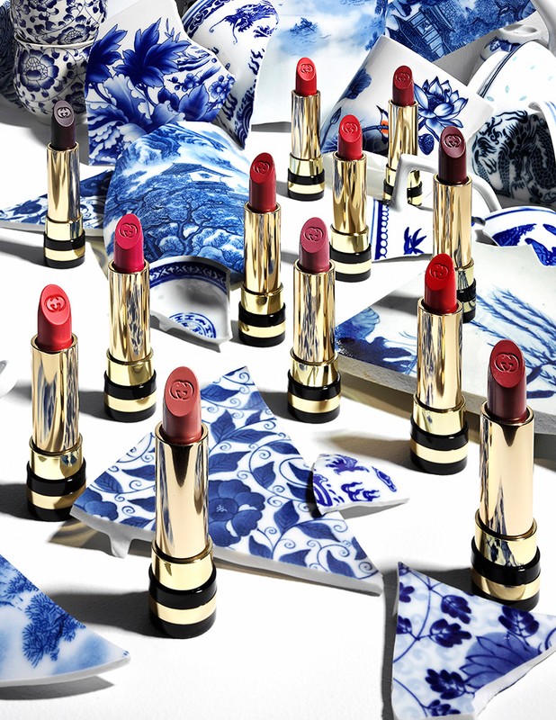 Close-up of several tubes of lipstick, arranged artfully on a white surface amid shattered pieces of blue and white porcelain.