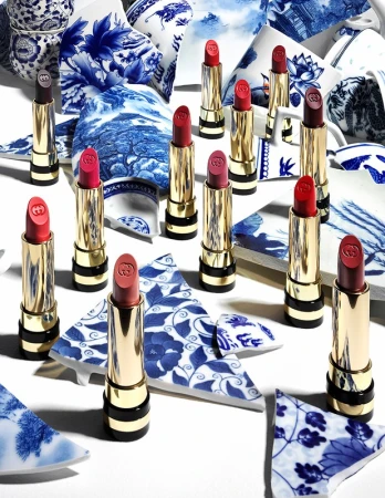 Close-up of several tubes of lipstick, arranged artfully on a white surface amid shattered pieces of blue and white porcelain.