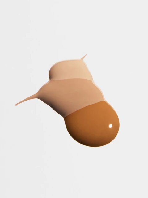Close-up studio shot of a smear of liquid foundation in various skin tones, including light, medium, and dark, against a white backdrop.