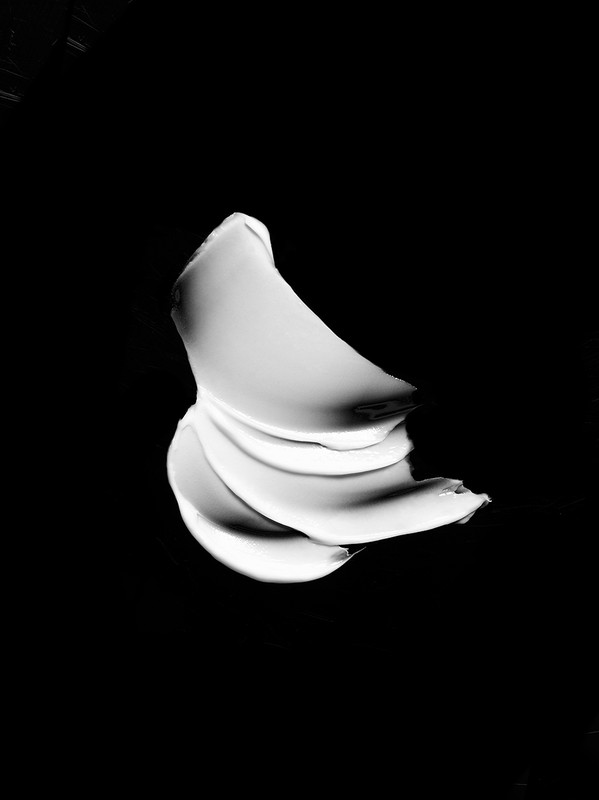Abstract monochrome shot of a thick, white cream or lotion swirl against a stark black backdrop, emphasizing texture and contrast.