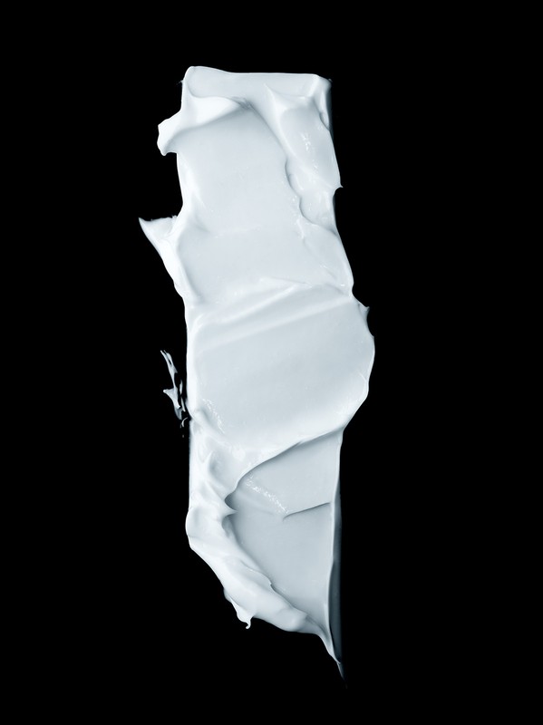 Close-up of a vertically aligned smear of a light-blue creamy substance, possibly cosmetic or skincare product, against a black backdrop.