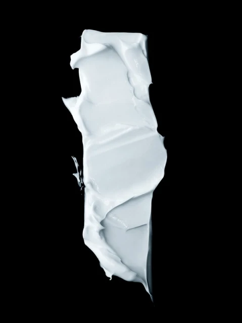 Close-up of a vertically aligned smear of a light-blue creamy substance, possibly cosmetic or skincare product, against a black backdrop.