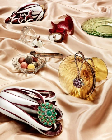 Still life of radicchio, jewelry, and dishware on a beige satin background, with green, gold, and purple jewel tones.
