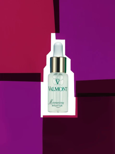 Valmont Moisturizing Booster serum bottle on a background of purple, magenta, and white geometric shapes, creating a modern beauty product shot.