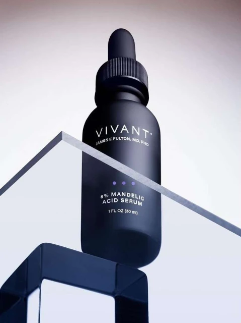 Vivant skincare product bottle on a geometric glass and dark blue plastic stand against a soft gradient background, product still life.