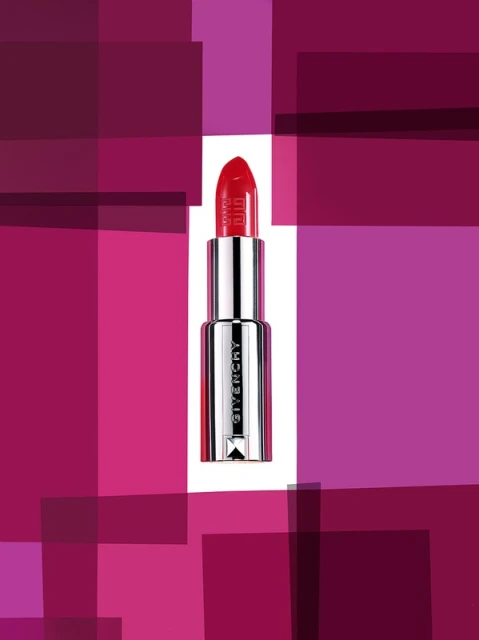 Close-up studio shot of red Givenchy lipstick with silver casing against a background of purple and pink abstract squares.