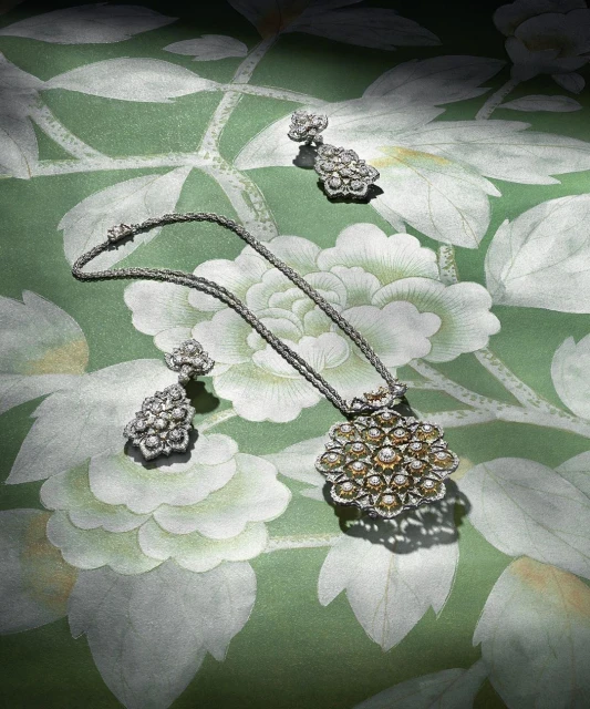Elegant jewelry set featuring a floral-inspired pendant necklace and drop earrings, displayed on a green floral patterned surface.