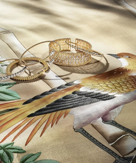 Close-up of three gold bracelets with bird pattern in the background. The bracelets are laid out on a patterned surface with a bird.