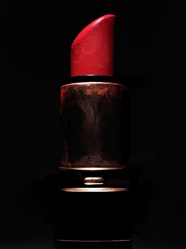 Close-up studio shot of vibrant red lipstick with gold casing against a stark black background, creating a bold and dramatic contrast.