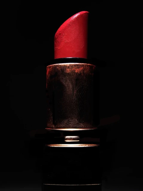 Close-up studio shot of vibrant red lipstick with gold casing against a stark black background, creating a bold and dramatic contrast.