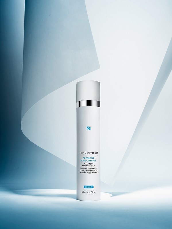 Studio shot of SkinCeuticals Advanced Scar Control, a white bottle with a silver accent on a blue and white geometric backdrop.