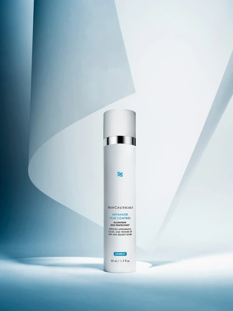 Studio shot of SkinCeuticals Advanced Scar Control, a white bottle with a silver accent on a blue and white geometric backdrop.