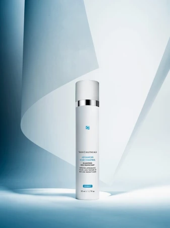 Studio shot of SkinCeuticals Advanced Scar Control, a white bottle with a silver accent on a blue and white geometric backdrop.