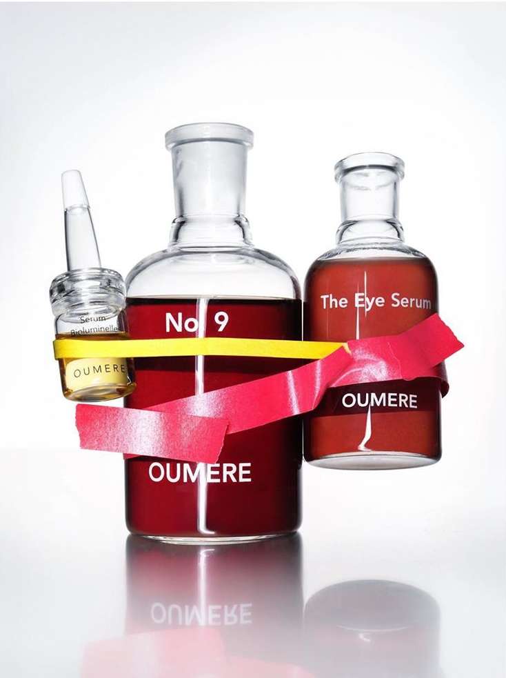 Three skincare bottles of different shapes with red and yellow ribbons on a white background. OUMERE brand visible on all bottles.