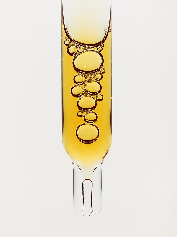 Close-up of a transparent glass pipette filled with golden liquid with bubbles on a plain white background, pharmaceutical or beauty product.
