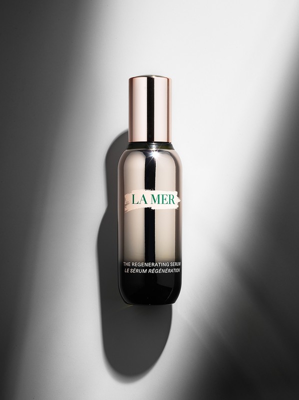 La Mer regenerating serum bottle with a silver and rose gold color scheme on a neutral gray background with dynamic lighting.