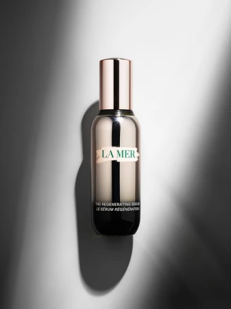 La Mer regenerating serum bottle with a silver and rose gold color scheme on a neutral gray background with dynamic lighting.