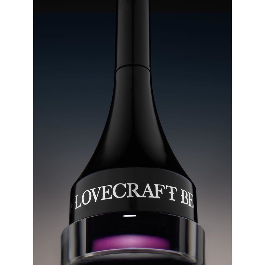 Close-up studio shot of a black cosmetic container with purple liquid at the base. The brand name 'LOVECRAFT BE' is displayed.