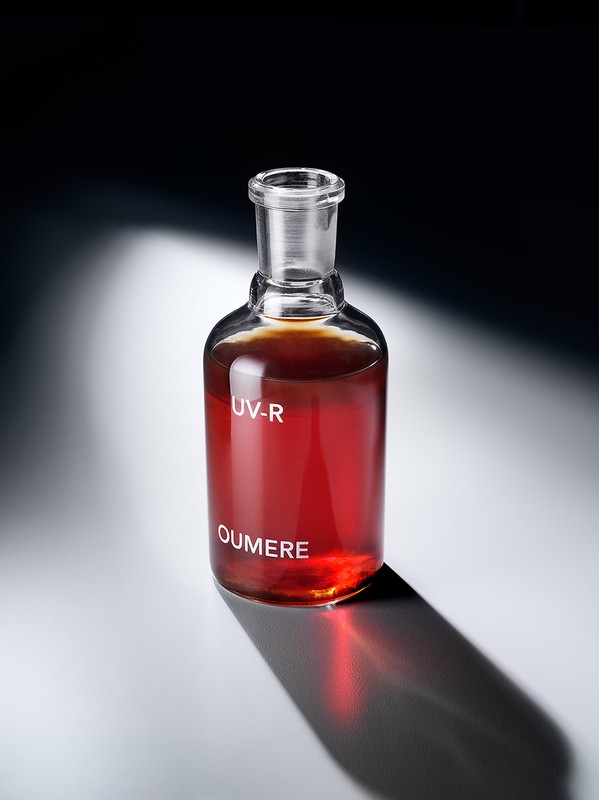 Laboratory flask with dark amber liquid on a white surface. Shadow cast behind the flask. White text 'UV-R' and 'OUMERE' on bottle.