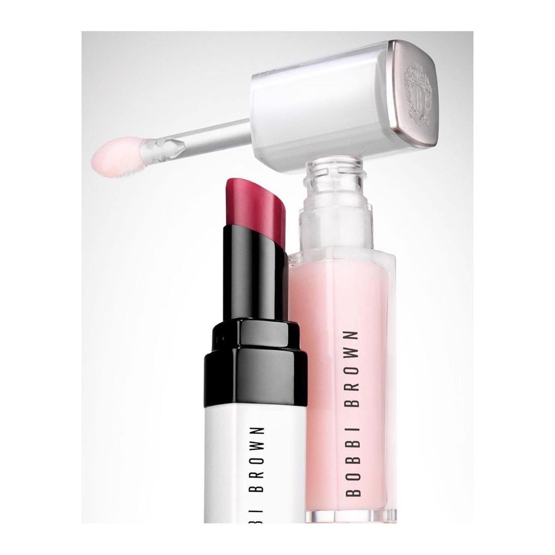 Close-up studio shot of a pink lip gloss tube and a red lipstick tube by Bobbi Brown cosmetics, against a white background.