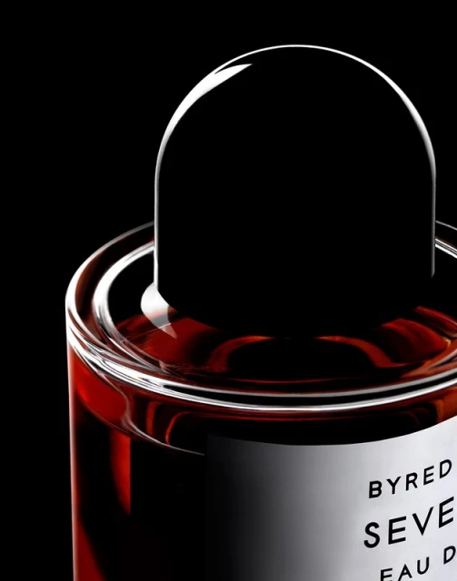 Close-up studio shot of Byredo Seven Veils perfume bottle with a dark brown liquid and a black rounded cap against black backdrop.