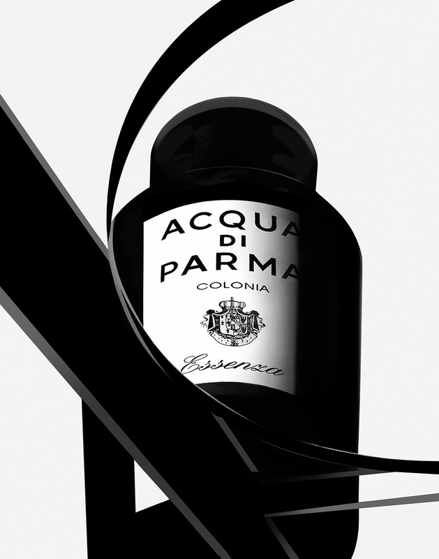 Elegant black and white studio shot of Acqua di Parma Colonia Essenza bottle with a fluid black ribbon accent on a white backdrop.