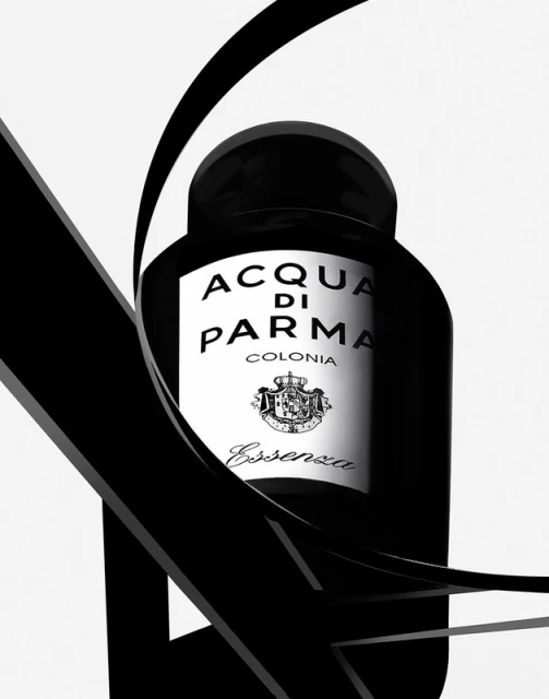 Elegant black and white studio shot of Acqua di Parma Colonia Essenza bottle with a fluid black ribbon accent on a white backdrop.