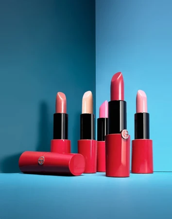Five pink and nude lipsticks in bright red tubes arranged against a solid blue background corner.