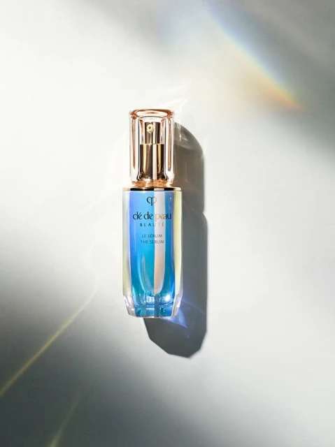 Cle de Peau Beaute Le Serum bottle on a white surface with rainbow light. Luxurious skincare product shot with minimalist composition.