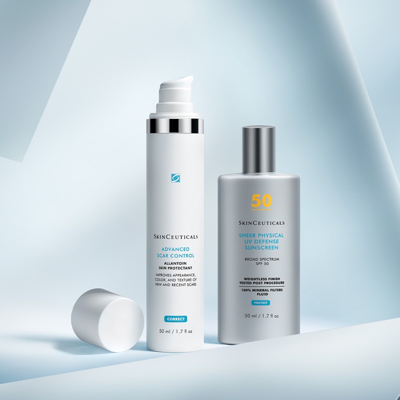 Two SkinCeuticals bottles stand on a light blue surface with abstract geometric background, one labeled scar control, one sunscreen.