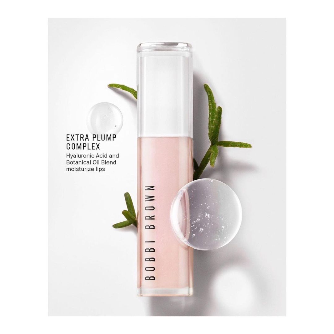 Bobbi Brown Extra Plump Complex lip gloss in a clear tube with botanical accents and a drop of serum, studio shot, light background.