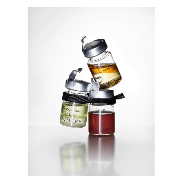 Three small clear bottles of cosmetic serums stacked on top of each other with black ribbon around the bottle necks on white.