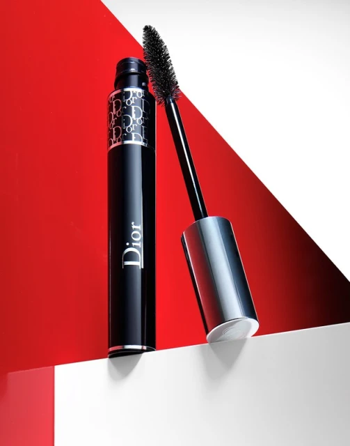 High-angle shot of Dior mascara tube and applicator wand against a white and red backdrop in a beauty and cosmetics studio.