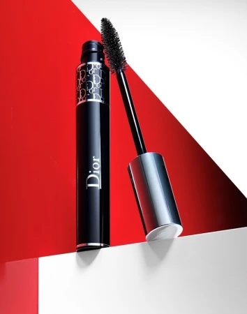 High-angle shot of Dior mascara tube and applicator wand against a white and red backdrop in a beauty and cosmetics studio.