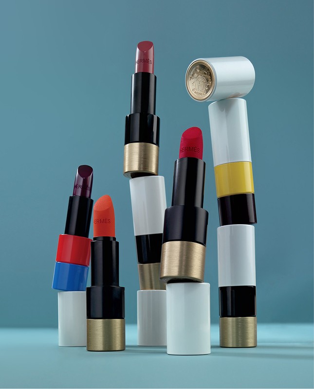Arrangement of colourful Hermes lipstick tubes against a blue background, with varied shades and textures creating a beauty still life.