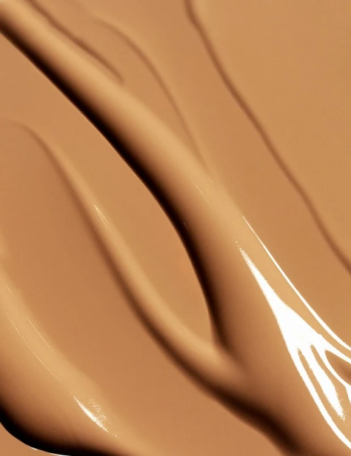 Macro close-up shot of tan-colored cosmetic foundation swatches with a glossy sheen. Beauty product background for makeup concepts.