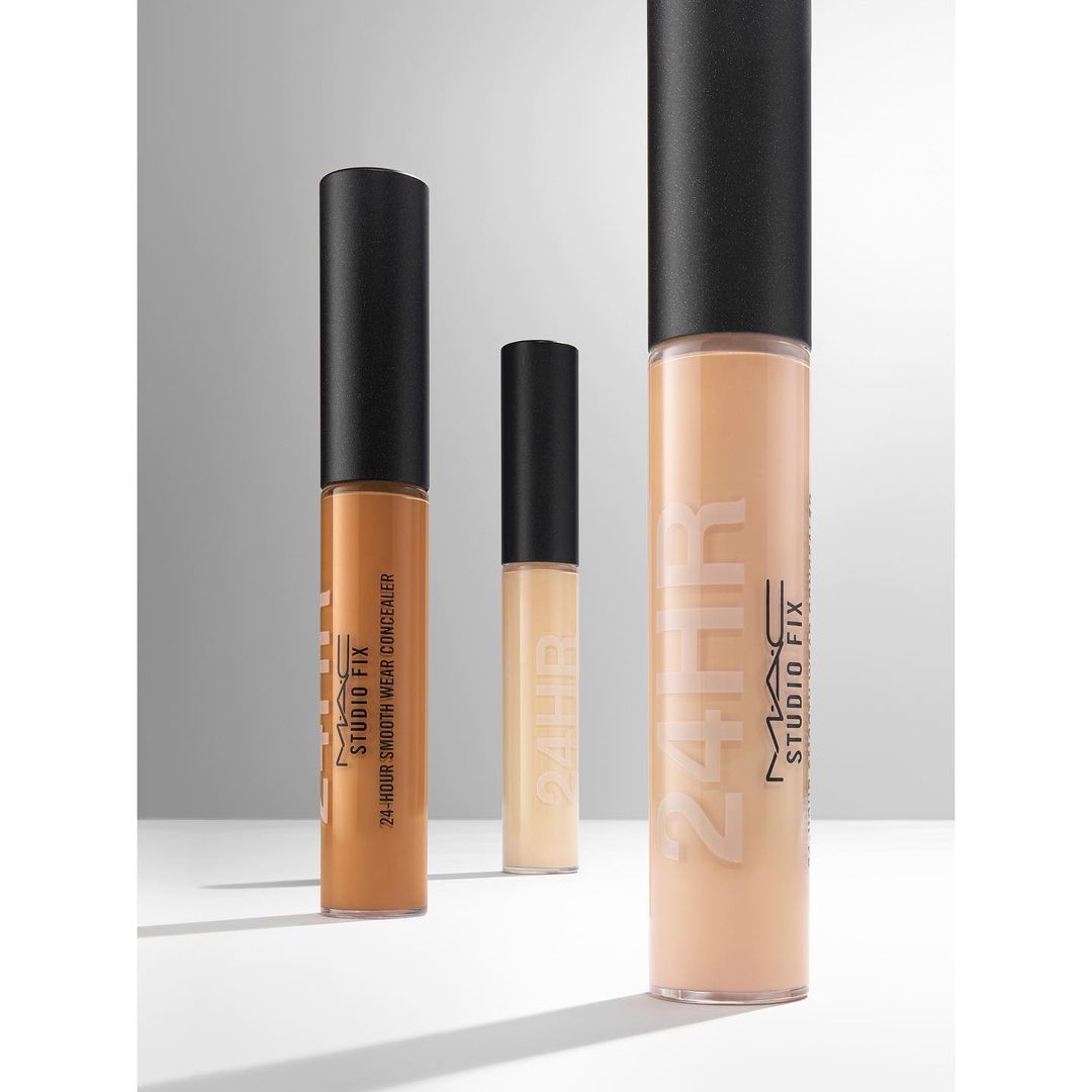 Three MAC Studio Fix concealers in varying shades are arranged against a neutral gradient backdrop in a beauty product shot.
