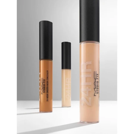 Three MAC Studio Fix concealers in varying shades are arranged against a neutral gradient backdrop in a beauty product shot.