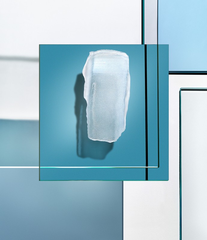 Close-up studio shot of semi-transparent ice chunk casting a soft shadow, against an abstract, layered geometric background in cool tones.