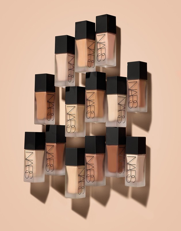 An array of NARS foundation bottles with varying shades, displayed on a neutral background, showcases beauty and cosmetic variety.