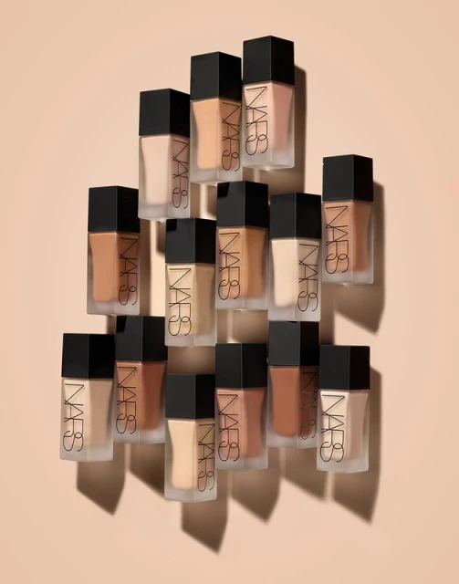 An array of NARS foundation bottles with varying shades, displayed on a neutral background, showcases beauty and cosmetic variety.