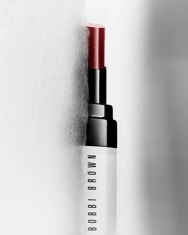 Close-up studio shot of a Bobbi Brown lipstick tube featuring a dark red lipstick bullet partially extended from the black and white container.