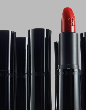 Close-up product photograph of a bright red lipstick tube standing out among several black capped lipsticks against grey
