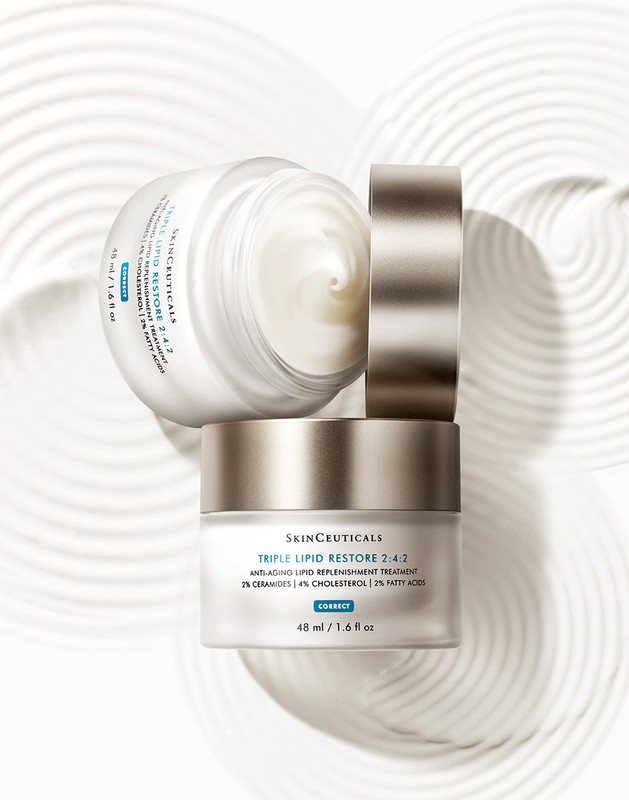 Elevated product shot of stacked SkinCeuticals Triple Lipid Restore jars on a light surface with concentric circle patterns for beauty advertising.
