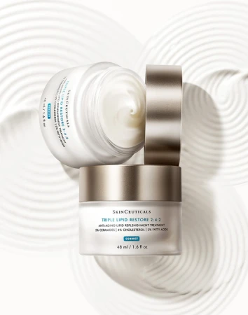 Elevated product shot of stacked SkinCeuticals Triple Lipid Restore jars on a light surface with concentric circle patterns for beauty advertising.