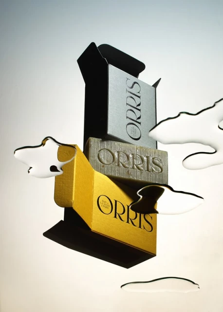 Three bars of Orris soap stacked in a tower, surrounded by pools of water on a gradient white to grey background in studio lighting.