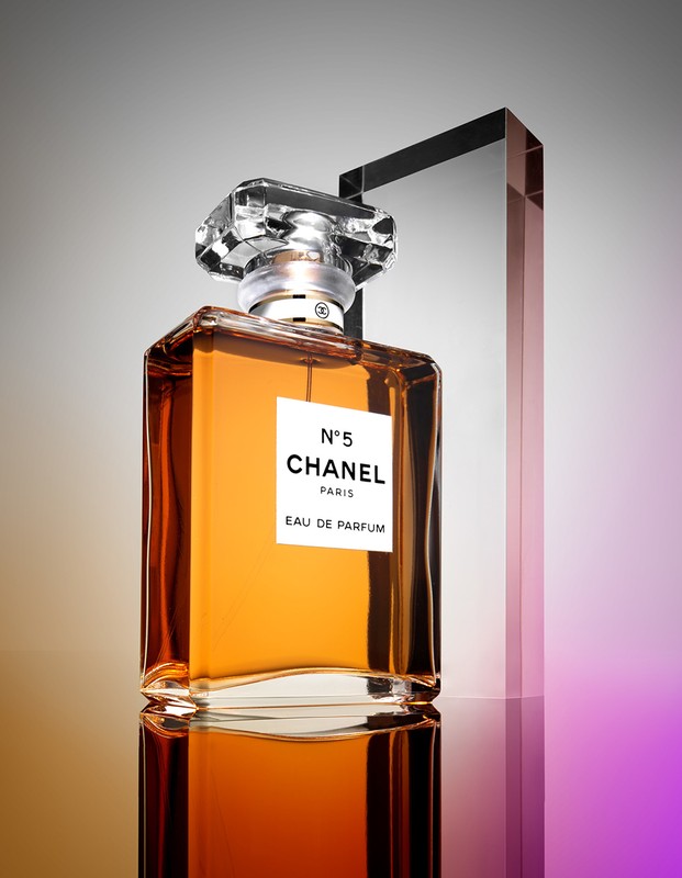 Elegant studio shot of Chanel N°5 perfume bottle with clear crystal stopper and amber liquid, set against a gradient backdrop.