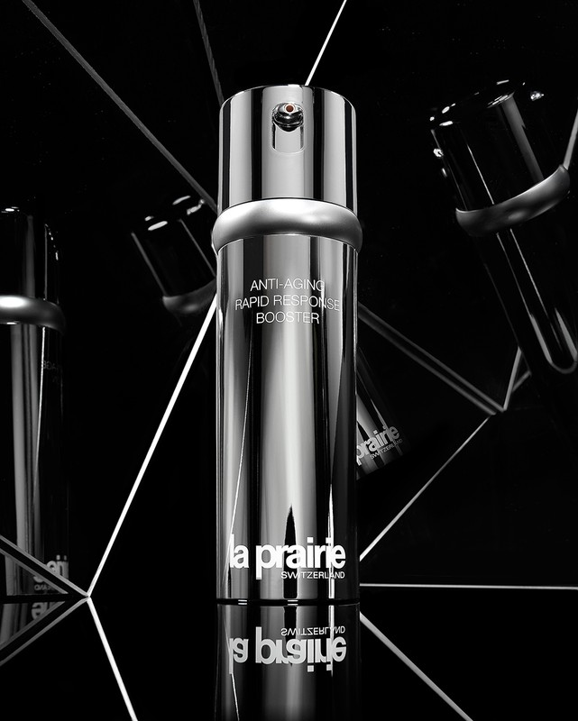 La Prairie silver skincare bottle with reflective surfaces, angled lighting, and a black background for a luxurious aesthetic.