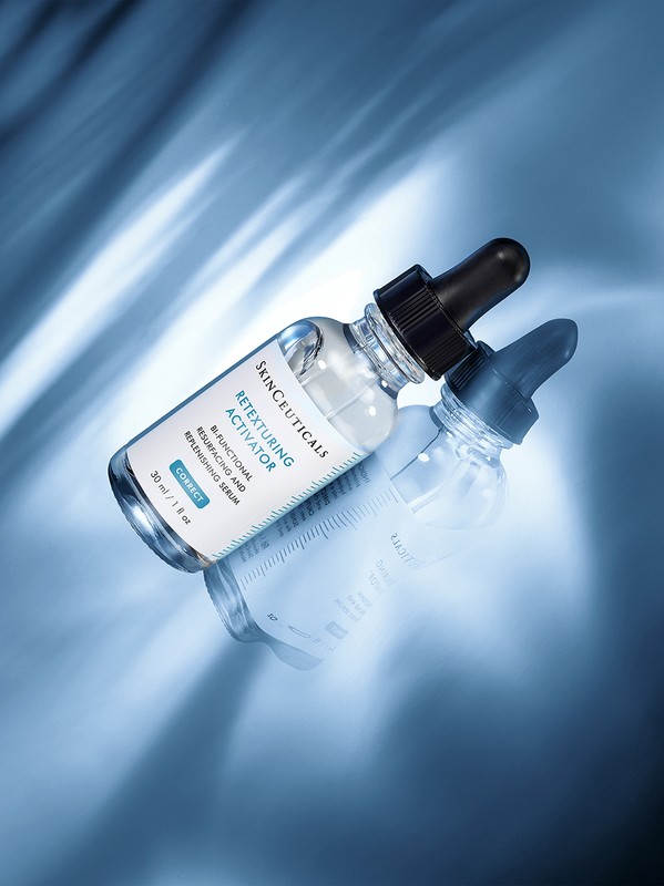Close-up of a clear glass bottle with a black dropper on a reflective surface, featuring the SkinCeuticals Retexturing Activator serum.