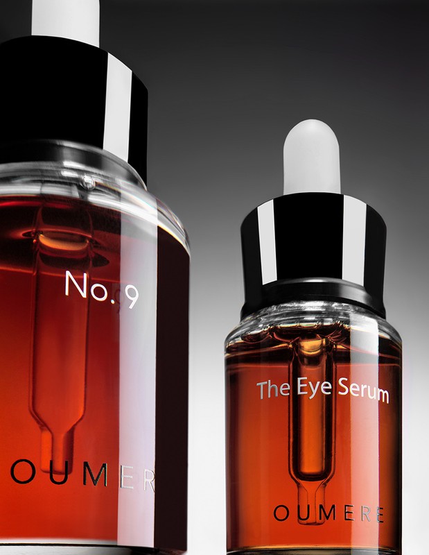 Close-up studio shot of two transparent glass dropper bottles filled with amber serum and labeled 'No. 9' and 'The Eye Serum.'